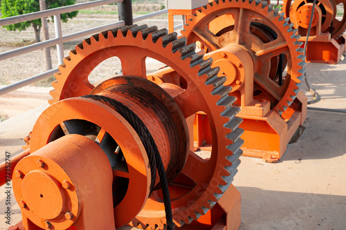 The orange gears of a large machine turn the wire rope.