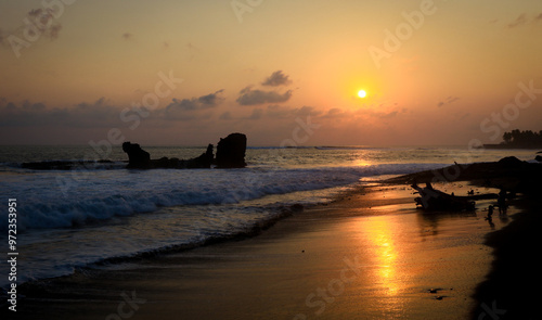 Sunset at El Tunco beach in El Salvador with waves crashing and silhouettes of rocks under vibrant sky