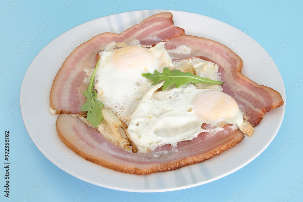 Fried eggs with bacon on a blue background close-up Fried eggs with bacon on a blue background close-up