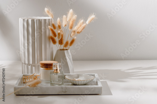 Marble tray with feminine accessories and perfume, ceramic vase at the background on white table with aesthetic sunlight shadows.