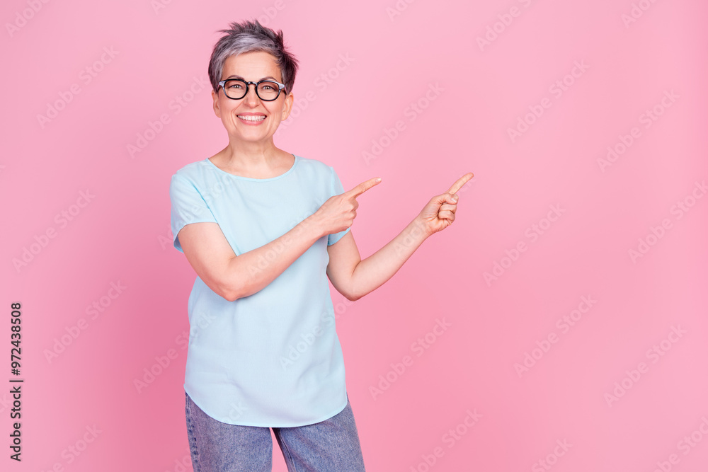 Photo of nice aged woman indicate fingers empty space blue t-shirt isolated on pink color background Photo of nice aged woman indicate fingers empty space blue t-shirt isolated on pink color background
