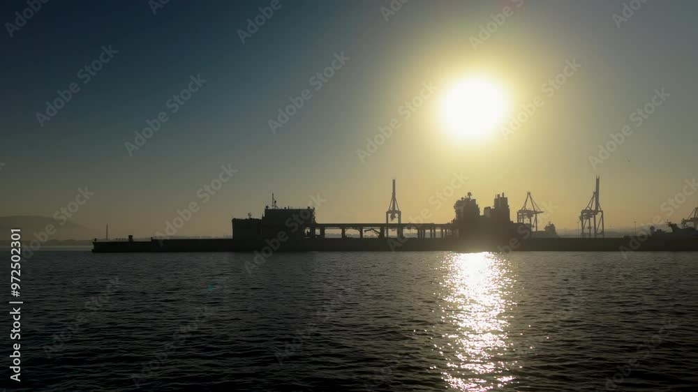 Silhouette of a harbor with cranes against a setting sun, reflecting on the water Silhouette of a harbor with cranes against a setting sun, reflecting on the water