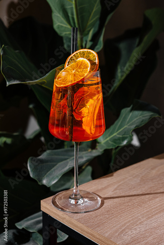 Refreshing aperol spritz cocktail standing on a table with tropical plants in the background