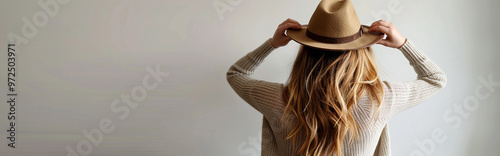 Woman Wearing Brown Hat with Long Wavy Hair in Cozy Sweater Facing White Wall