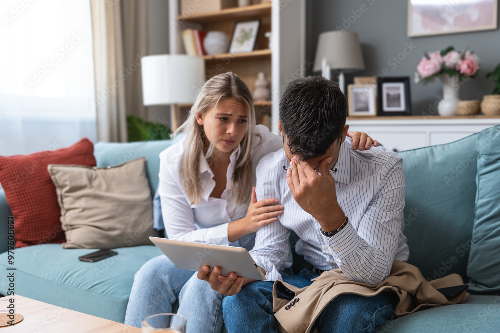 Young businesswoman comforting her husband at home while he reading negative statistics of his business company trade on digital tablet. Togetherness and emotional support. Young businesswoman comforting her husband at home while he reading negative statistics of his business company trade on digital tablet. Togetherness and emotional support.