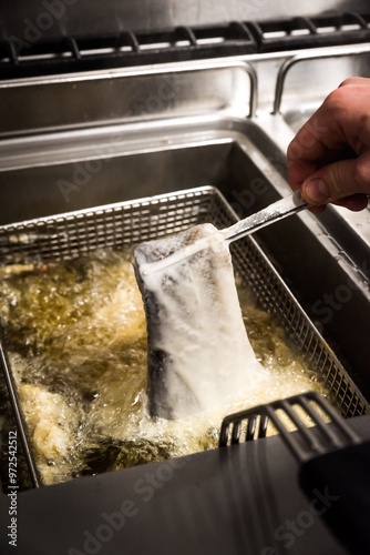 A fish fillet in batter being dipped into deep fat fryer in restaurant kitchen