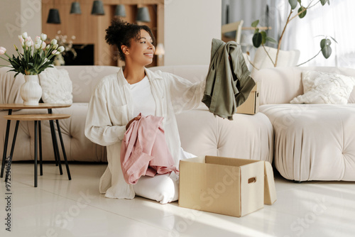 Canvas Print Young woman organizing clothes in cardboard boxes at home