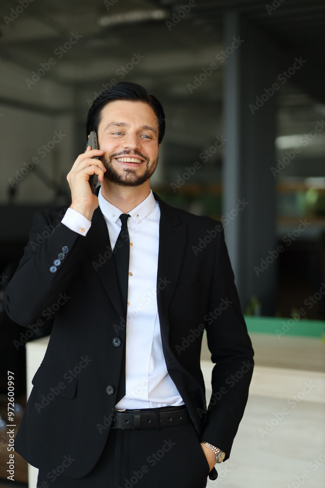 A man in a suit is talking on his cell phone. He is smiling and he is in a good mood A man in a suit is talking on his cell phone. He is smiling and he is in a good mood