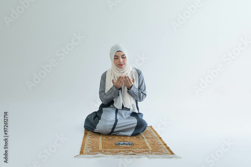 An Asian Muslim woman sits on a carpet in a white room and prays for a blessing that Muslims believe God grants to individuals and believers in Islam. photo