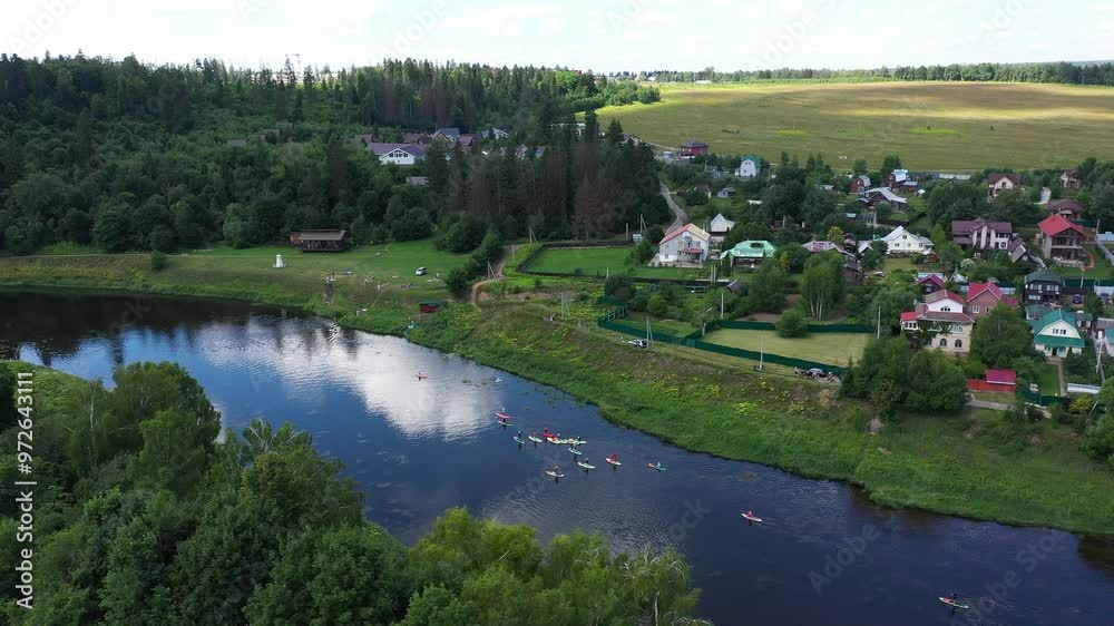 People on SUP boards raft on river among greenery and houses, top panoramic view People on SUP boards raft on river among greenery and houses, top panoramic view