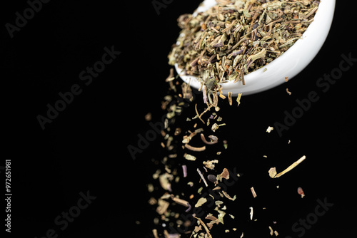 Fototapeta Naklejka Na Ścianę i Meble -  Seasoning dried crushed basil leaves pouring on a black background space for text