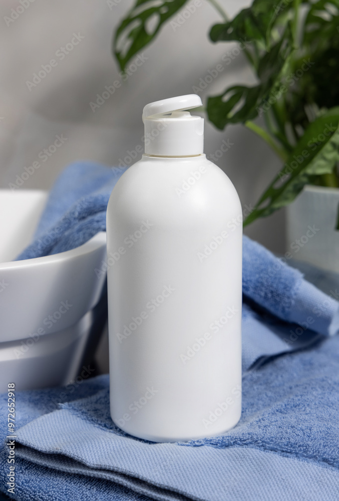 White cosmetic flip cap bottle on blue towels near green plant and basin in bathroom, mockup White cosmetic flip cap bottle on blue towels near green plant and basin in bathroom, mockup