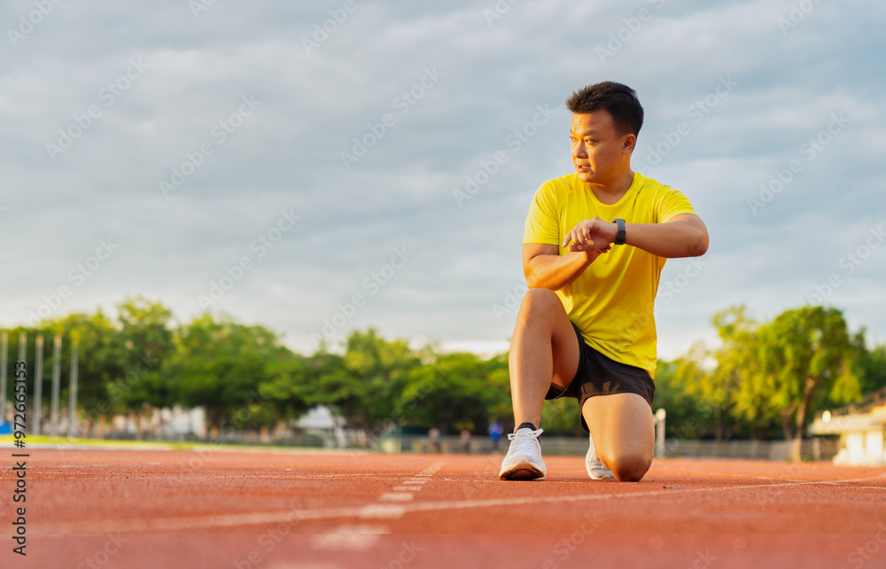 Fototapeta premium Male runner using smartwatch to track workout progress on the running track