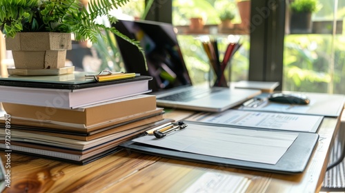 Closeup of a wooden desk with books, laptop, clipboard, and pencils.