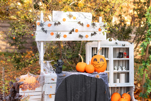 Halloween orange pumpkin head jack lantern with statuette cat bat. Festive composition on table decorated with pumpkins, bats, spiders, cobwebs and witch magic attributes. Halloween design decor home photo