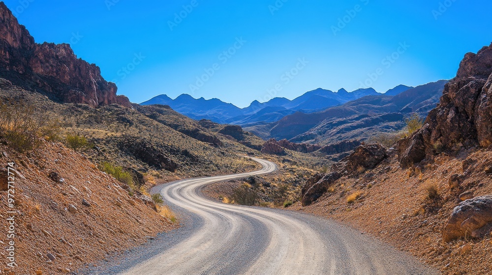 Winding dirt road through arid desert landscape under bright blue sky in southern Nevada during daylight hours Winding dirt road through arid desert landscape under bright blue sky in southern Nevada during daylight hours