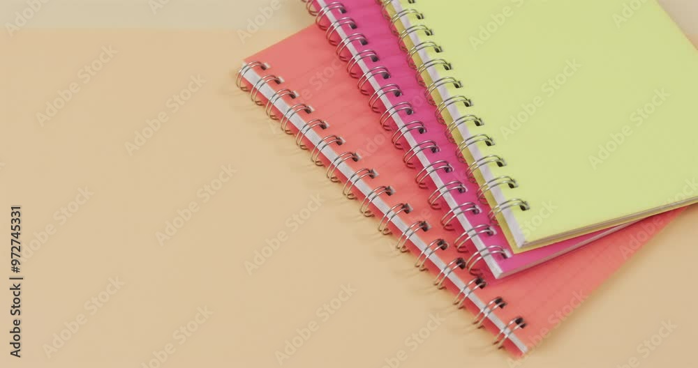 Colorful spiral notebooks are stacked on a dual-toned pink and yellow background, with copy space