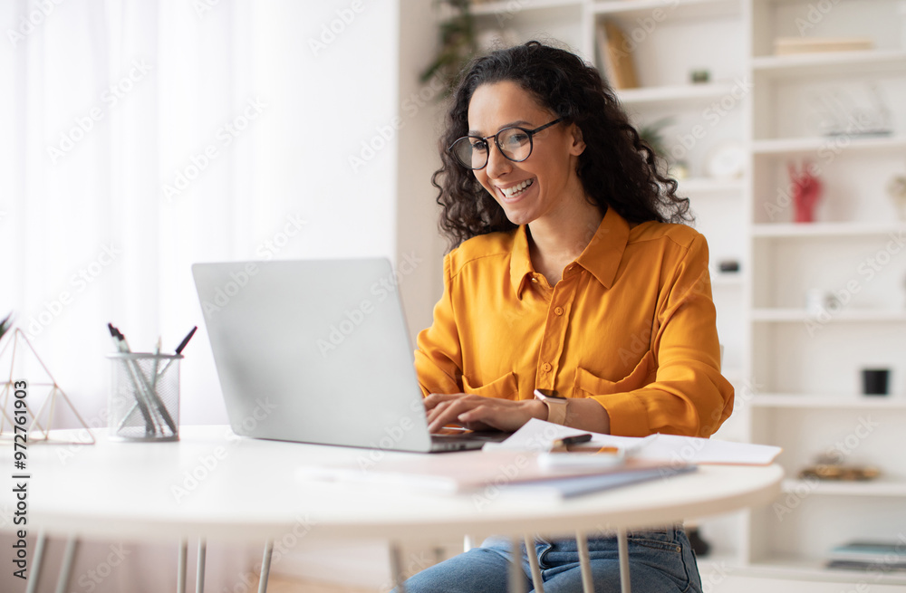 Happy Middle Eastern Businesswoman Using Laptop Typing And Working Online Sitting At Workplace Wearing Eyeglasses. Office Worker Lady Browsing Internet On Computer. Entrepreneurship. Side View Happy Middle Eastern Businesswoman Using Laptop Typing And Working Online Sitting At Workplace Wearing Eyeglasses. Office Worker Lady Browsing Internet On Computer. Entrepreneurship. Side View