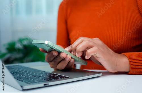 Woman hand with a mobile phone over a laptop, Workplace at home, freelancer, Working sitting in office at home, Online shopping and payments, Ecommerce and secure mobile banking concept.