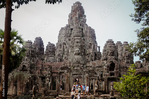 Visitors explore the ancient ruins of Angkor Wat in Cambodia amidst sprawling trees and intricate stone carvings