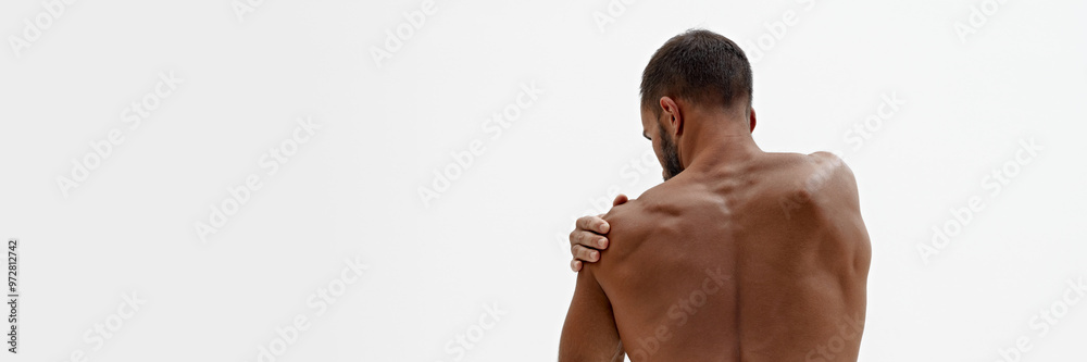 Banner. Rear view of man holding hand on shoulder as he feels pain in joints against white background with negative space. Concept of beauty and fashion, style and youth, male health. Banner. Rear view of man holding hand on shoulder as he feels pain in joints against white background with negative space. Concept of beauty and fashion, style and youth, male health.