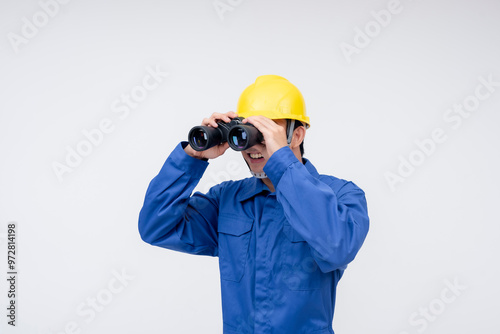 A worker in a blue uniform and yellow hard hat uses binoculars, suggesting supervision, observation, or lookout duties. Construction, safety, or maritime professions.