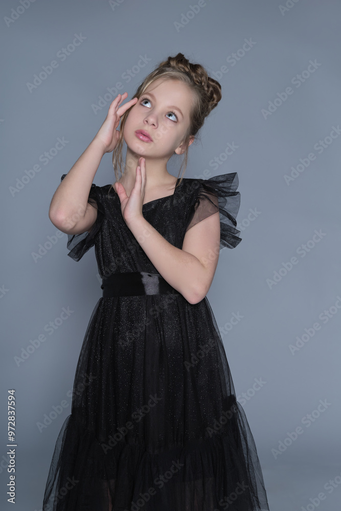A young girl strikes an elegant pose with her hands delicately near her face, wearing a black dress with tulle ruffles. This image highlights poise and sophistication in children's fashion, showcasing