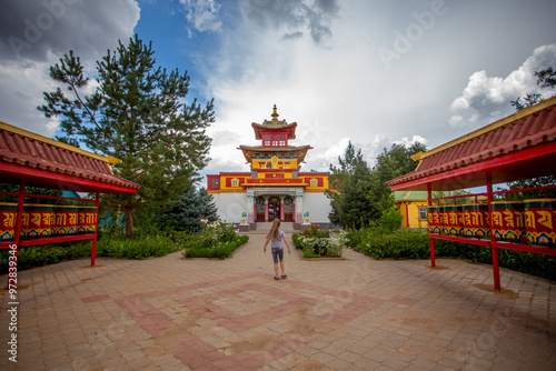 A landscape with a Buddhist temple. A beautiful white datsan.  Red prayer drums and a temple with a beautiful roof on a background of blue sky and clouds.