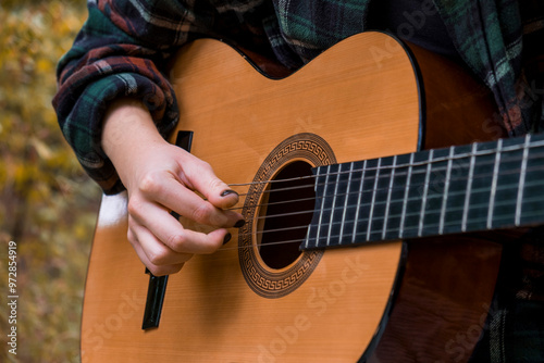 Teen girl playing guitar. Girl playing guitar in car. Autumn atmosphere. Car ride. Checkered shirt. Sun rays. Forest. Forest background. Car in forest photo