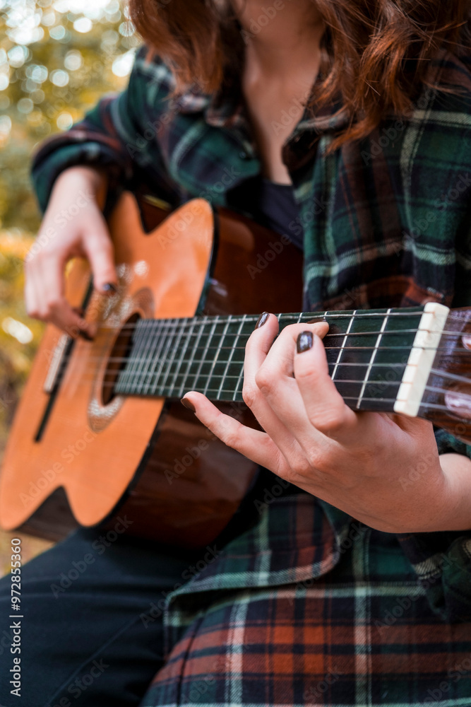 Fototapeta premium Teen girl playing guitar. Girl playing guitar in car. Autumn atmosphere. Car ride. Checkered shirt. Sun rays. Forest. Forest background. Car in forest
