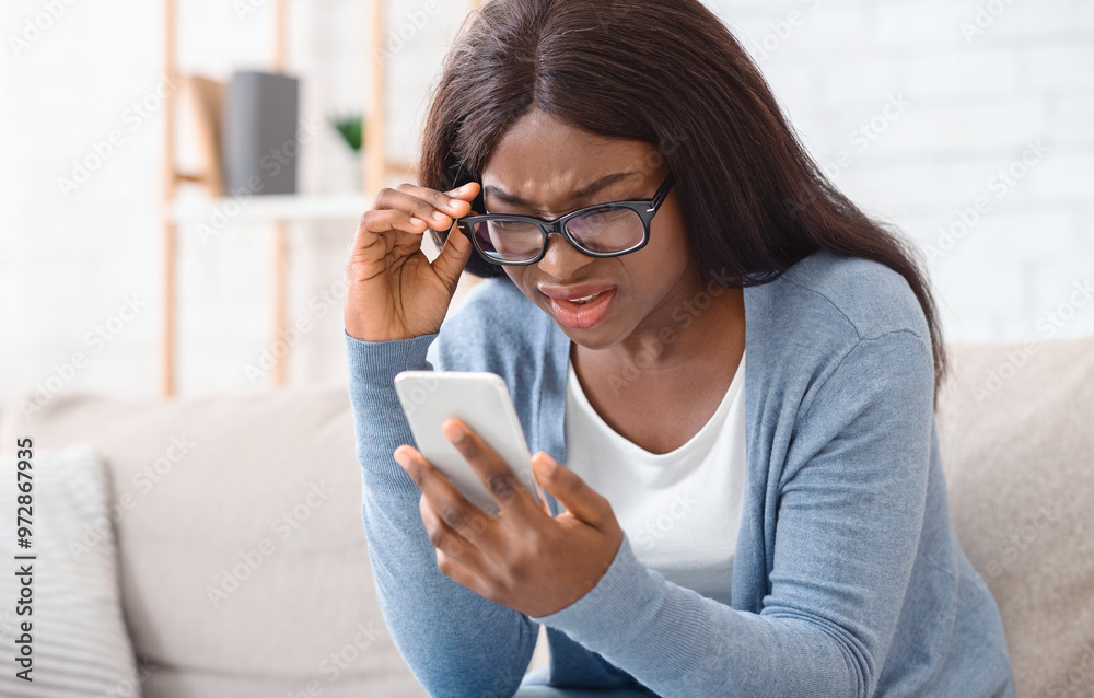 © Prostock-studio - Can not believe my eyes. Sceptical afro woman in eyeglasses reading unexpected message on smartphone, full of disbelieve or having vision problem
