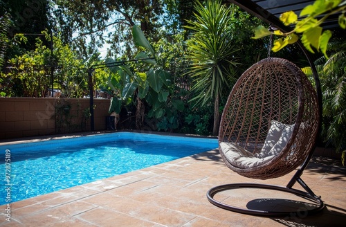In summer, luxurious pool in a private villa's garden, hanging chair filled with pillows for tourists. Portugal, Algarve.