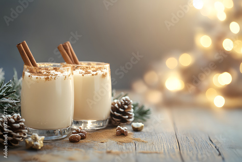Two elegant glasses filled with creamy holiday drinks are garnished with cinnamon sticks, surrounded by pinecones and a warm, glowing ambiance from festive lights.