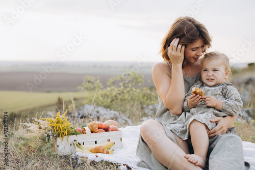 Mother and Child Enjoying a Serene Picnic in a Scenic Field with Apples and Croissants photo