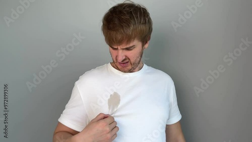 young handsome man in white t-shirt spilled coffee on his t-shirt. concept stained and dirty clothes, spot, gray background