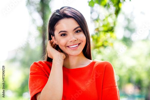 Photo of attractive teen cheerful girl tuck hair behind ear charming wear red garment having fun outside outdoors