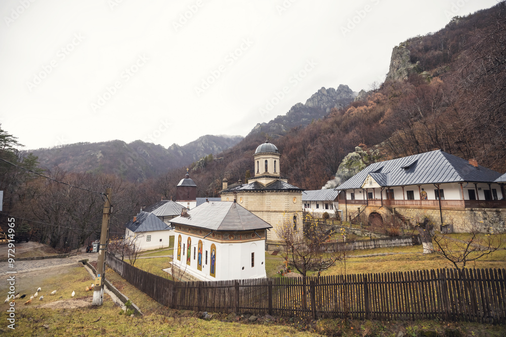 Fototapeta premium Amidst majestic mountains, a historic monastery reveals its beauty under soft clouds, surrounded by nature's tranquility, inviting quiet reflection and exploration