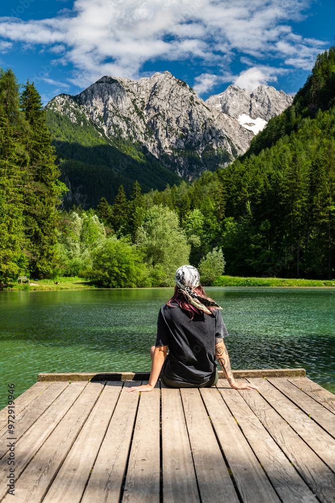 Active young woman sitting at Lake Plansar looking Alpine mountains peaks in Slovenia at summer Active young woman sitting at Lake Plansar looking Alpine mountains peaks in Slovenia at summer