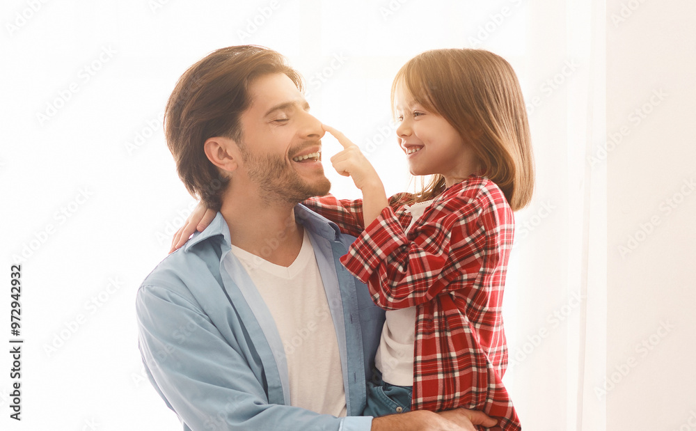 Portrait of cheerful father and little daughter bonding over white background at home, girl touching daddy nose Portrait of cheerful father and little daughter bonding over white background at home, girl touching daddy nose
