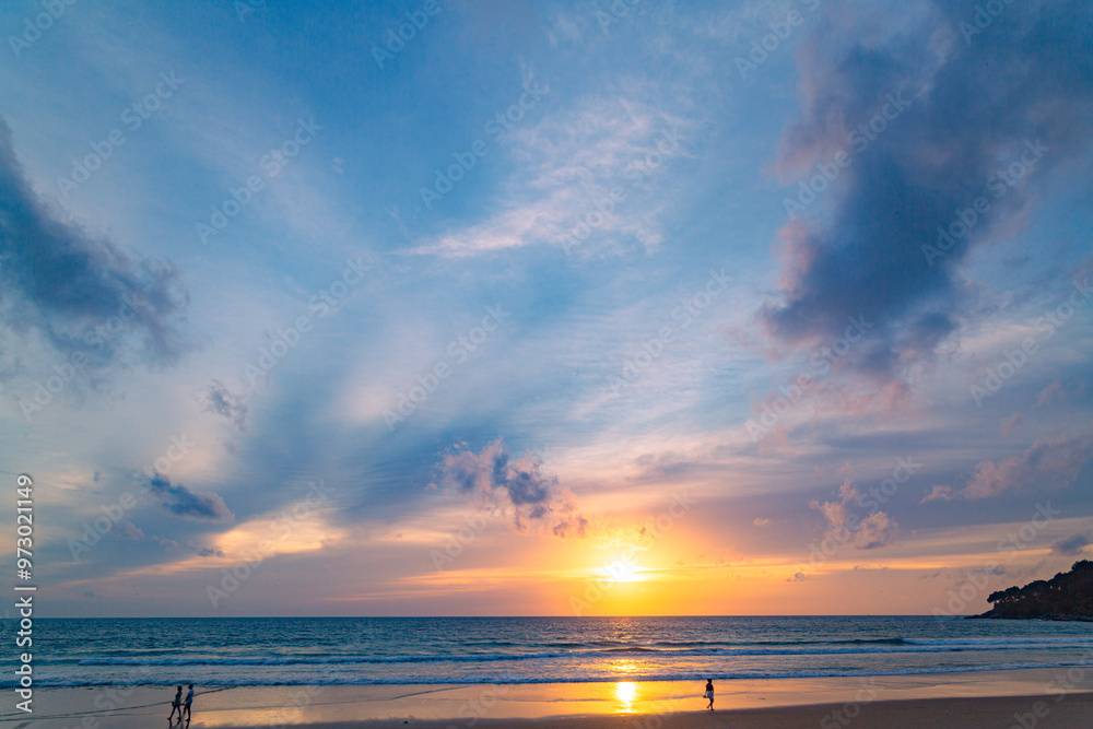 Obraz premium A stunning sunset over the ocean with soft golden light reflecting on the water, featuring silhouettes of people walking along the shore. Water flows from a small stream into the sea.