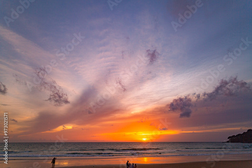 A serene beach scene at dusk, showcasing a vivid sunset with colorful clouds reflected on the calm waters and wet sand. amazing sky in sunset over Karon beach Phuket. sweet sky background.