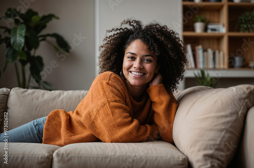 A happy afro american woman is relaxing on the sofa at home. Enjoying her day off by lying or sitting on the sofa