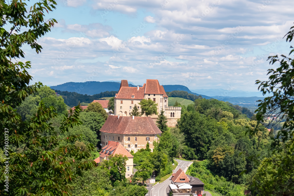 Fototapeta premium Panoramic view of historic Seggau castle on hill Seggauberg in Leibnitz, south west Styria, Austria, Europe. Idyllic landscape with trees and rolling hills. Peaceful serene atmosphere in summer