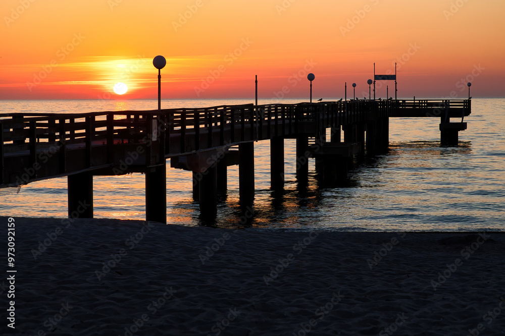 Orange sky and sun behind a pier at the Baltic Sea on a spring night in northern Germany at sunset. Orange sky and sun behind a pier at the Baltic Sea on a spring night in northern Germany at sunset.