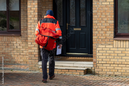 Fotografie Postman or Mailman in UK posting mail through the letter or mailbox of a house f