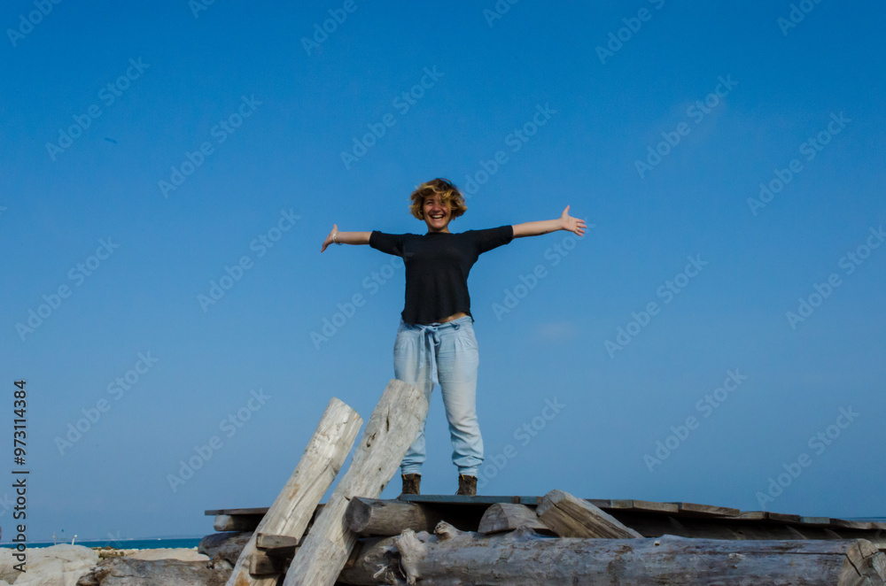 Una ragazza felice in piedi su alcuni scogli di fronte al mare allarga le braccia e sorride Una ragazza felice in piedi su alcuni scogli di fronte al mare allarga le braccia e sorride