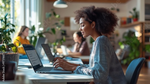 Young woman working on a laptop in a modern co-working space filled with greenery during daylight hours photo