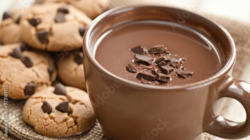 Rich hot chocolate in a brown cup topped with chocolate shavings, surrounded by freshly baked chocolate chip cookies, warm and inviting atmosphere perfect for relaxation and indulgence.