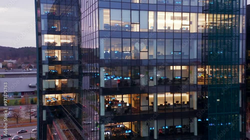 Drone offers a stunning view of a glass skyscraper, its office windows brightly lit by employees working into the late hours, reflecting the bustling energy of the corporate world. Drone offers a stunning view of a glass skyscraper, its office windows brightly lit by employees working into the late hours, reflecting the bustling energy of the corporate world.