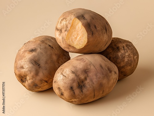 Close up of four raw potatoes, one with a bite taken out of it, on a tan background. photo